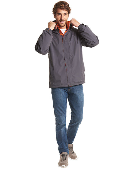 Person wearing Uneek Clothing UC621 - Deluxe Outdoor Jacket in deep grey with hood with fiery orange fleece lining, full front zip and flap with velcro.