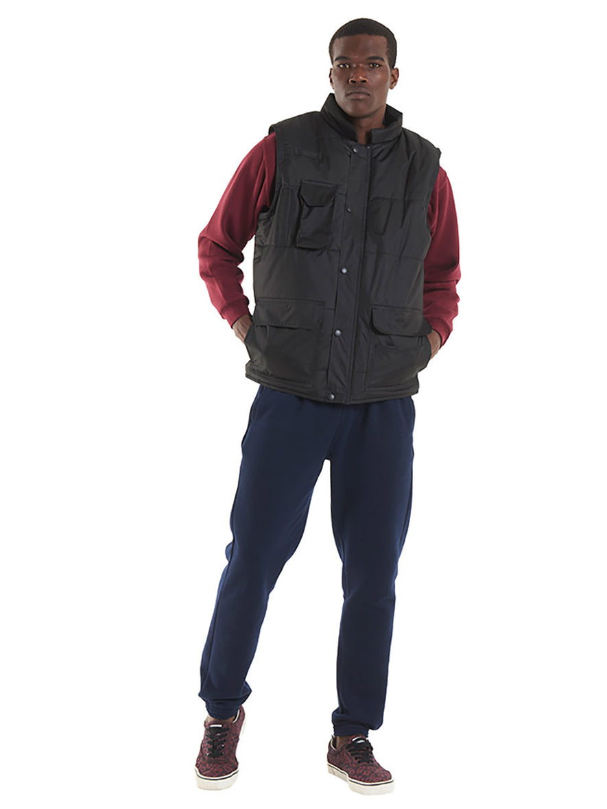 Person wearing Uneek Clothing UC640 -Super Pro Body Warmer padded with pockets on right chest and two on front with flaps in black.